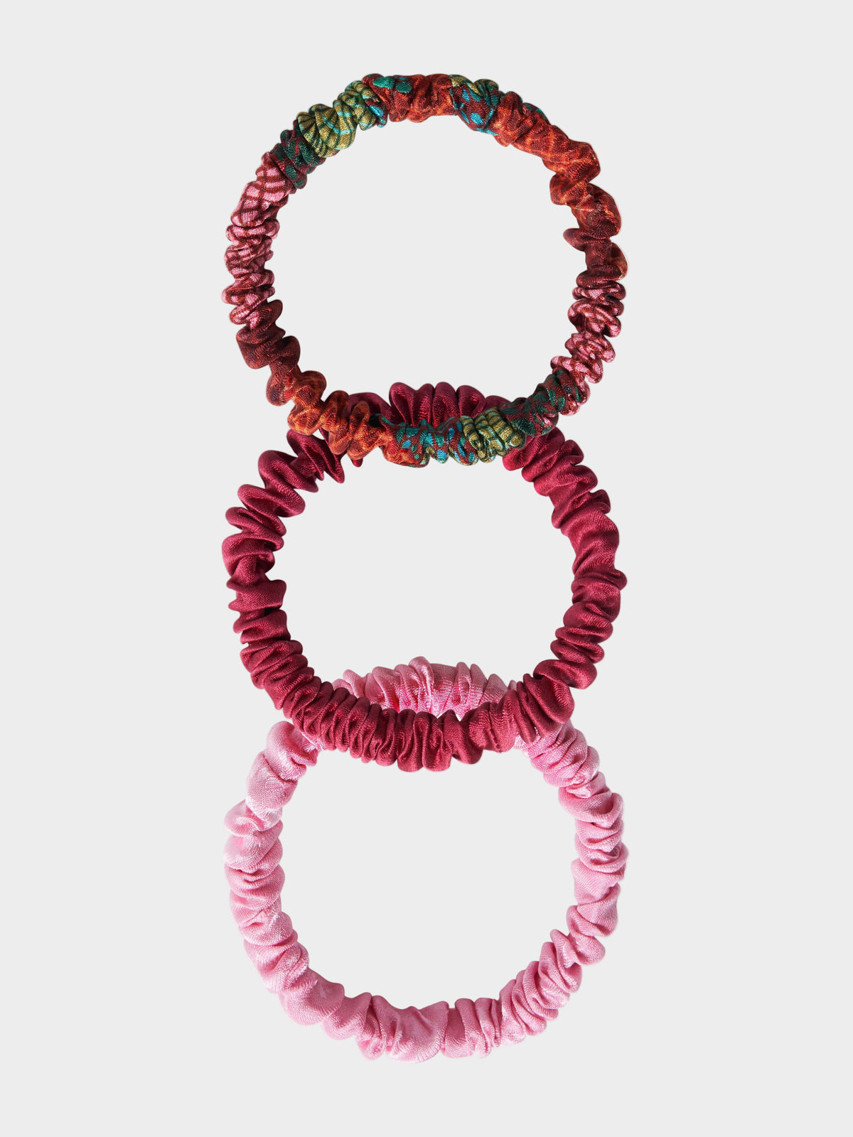A set of three silk scrunchies in pink colors with a textured pattern.